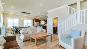 A spacious living room with a wooden coffee table, a beige sofa, and a white armchair. A staircase with white railings leads to an upper level. - Family Beach Escape Near Gulf and Bay (Cape San Blas)