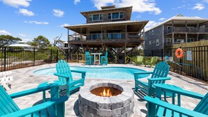 Ein Schwimmbad mit blauen Stühlen und einer Feuerstelle, umgeben von einer Holzterrasse und einem Gebäude mit mehreren Balkonen.