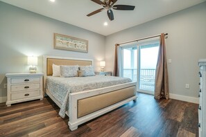 Quarto com cama, mesas de cabeceira, ventilador de teto, janela com cortinas e vista para o exterior.