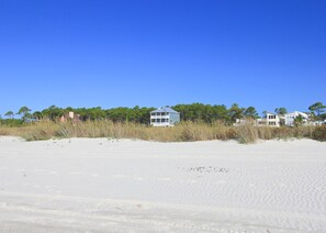 Um imóvel à beira-mar com várias casas, praia de areia e árvores densas ao fundo.
