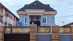 A two-story house with a gated entrance, stone pillars, and a tiled roof. - Tastefully furnished 2 bedroom apartment with 24/7 Power|WiFI|Security (Alimosho)
