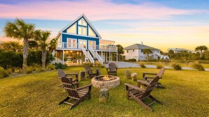 Een huis aan het strand met een terras, buitenmeubels en een vuurkuil.