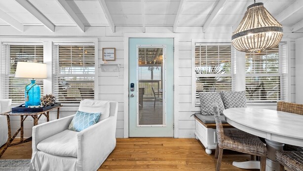 A room with a white door, a blue wall, a white sofa, a wicker chair, a round table, and a hanging light fixture. - Waterfront Cottage Near Beach Access (Cape San Blas)