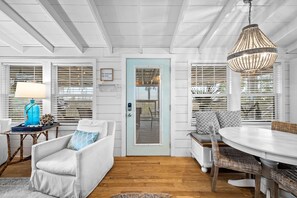 A room with a white door, a blue wall, a white sofa, a wicker chair, a round table, and a hanging light fixture.