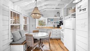 A kitchen with white cabinetry, a round dining table, wicker chairs, and a hanging light fixture. - Waterfront Cottage Near Beach Access (Cape San Blas)