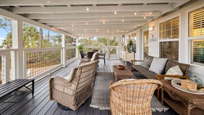 A covered outdoor seating area with wicker furniture, a wooden bench, and a view of the surrounding landscape. - Waterfront Cottage Near Beach Access (Cape San Blas)