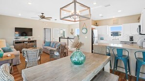 A spacious living room with a wooden dining table, wicker chairs, and a large green vase.