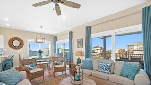 A spacious living room with a large window, a ceiling fan, and a view of the ocean.