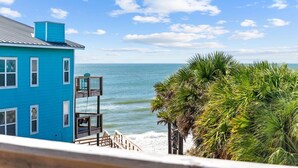 A blue building with a dock extending to a beach, palm trees, and a clear view of the ocean.