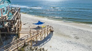 Ein Gebäude direkt am Strand mit einer Holzterrasse, einem blauen Sonnenschirm und einer Treppe zum Strand.