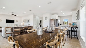 Un comedor amplio con una mesa y sillas de madera, una cocina con armarios blancos y un ventanal grande.
