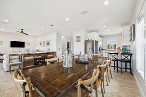 A spacious dining area with a wooden table and chairs, a kitchen with white cabinets, and a large window. - Vista Blue - Gulf-Front Home with Private Beach Access and Sweeping Views! (Indian Pass)