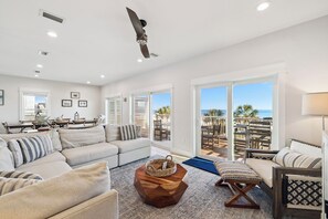 A spacious living room with a large sofa, a coffee table, and a view of the ocean through sliding glass doors.