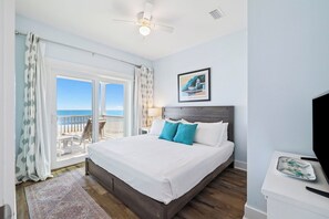 A bedroom with a bed, a ceiling fan, a view of the ocean, a framed picture on the wall, and a small table with a tray.
