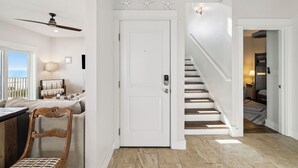Un pasillo con una puerta blanca, una escalera y vistas a un balcón.