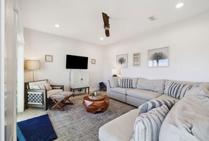 A living room with a sofa, a coffee table, a TV, and a ceiling fan. - Vista Blue - Gulf-Front Home with Private Beach Access and Sweeping Views! (Indian Pass)