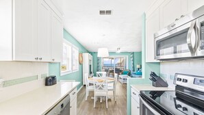 Een keuken met witte kasten, een vaatwasser, een magnetron en een oven. Er is een eethoek met een tafel en stoelen.