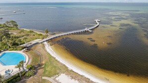 An aerial view of a coastal area with a long pier extending into the water, a swimming pool, and a beach.