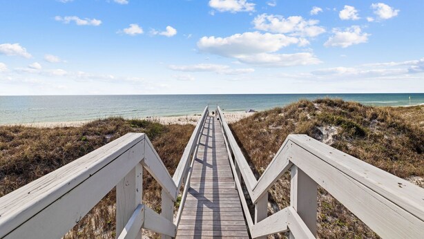 A wooden boardwalk leading to a beach with a clear sky and clouds.