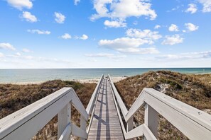 En träpromenad som leder till en strand med klar himmel och moln.