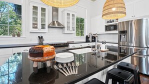 Una cocina moderna con armarios blancos, electrodomésticos de acero inoxidable, una isla grande con un pastel y luminarias colgantes.