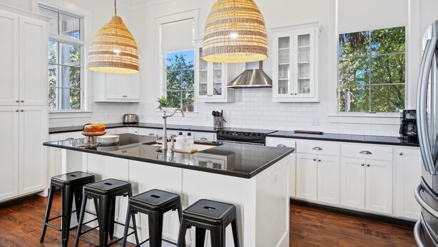 Una cocina moderna con armarios blancos, una isla central con taburetes e iluminación colgante.
