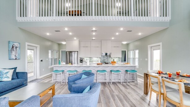 A spacious living area with a high ceiling, a kitchen with white cabinets, and a dining area with wooden chairs. - Beach Retreat w/Pool and Foosball (Port St. Joe)