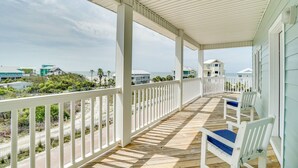 A covered porch with white railings, wooden floor, and blue cushioned chairs. - Beach Retreat w/Pool and Foosball (Port St. Joe)