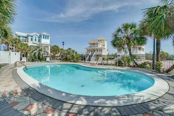 A swimming pool surrounded by palm trees and a two-story building with a balcony.