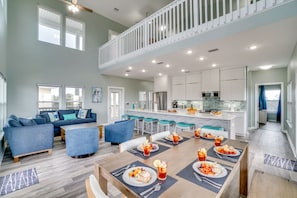 A spacious living area with a dining table set for a meal, a kitchen with modern appliances, and a balcony with a railing.