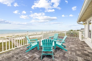 A wooden deck with Adirondack chairs overlooking a beach.