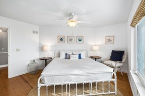 A bedroom with a bed, two bedside tables, a ceiling fan, and framed pictures on the wall.