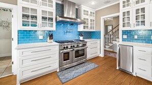 A modern kitchen with white cabinetry, a stainless steel range, and blue-tiled backsplash.