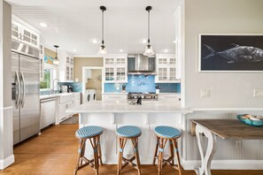 A modern kitchen with white cabinetry, a central island with stools, and a large window.