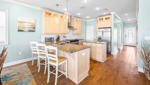A modern kitchen with wooden cabinets, a central island, and a dining area with white chairs.