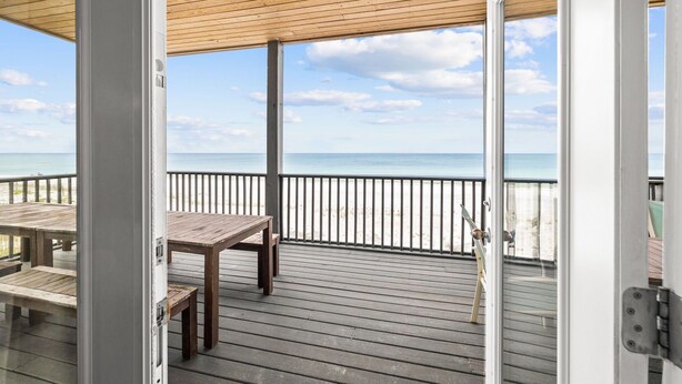 A wooden deck with a table and benches, overlooking a beach with a clear sky.