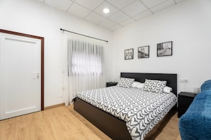 A bedroom with a bed, a nightstand, a blue chair, and three framed pictures on the wall.