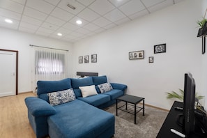A living room with a blue sofa, a small table, a TV, and framed pictures on the wall.