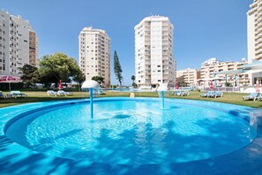A swimming pool with lounge chairs, surrounded by tall residential buildings.