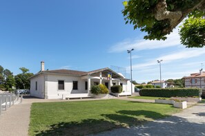 Un bâtiment blanc avec un toit en tuiles, un petit jardin et un mât sur lequel flottent des drapeaux.