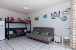 Quarto com beliches, sofá, pequena mesa, geladeira e quadros nas paredes.