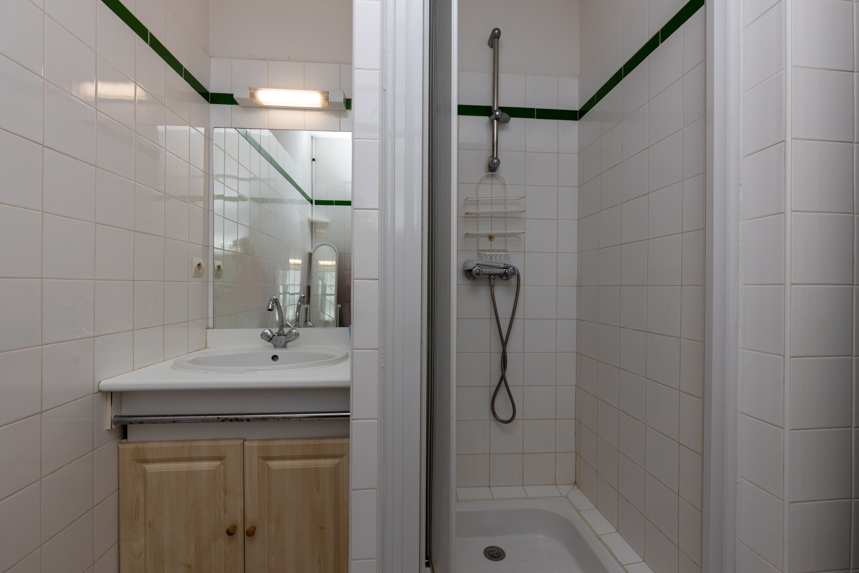 Un baño con lavamanos, espejo, armarios de madera y zona de ducha.