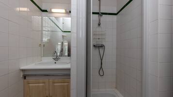 Un baño con lavamanos, espejo, armarios de madera y zona de ducha.