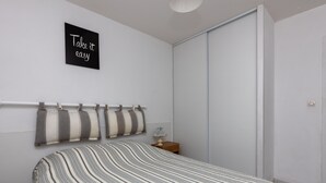 Ein Schlafzimmer mit Bett, Nachttisch mit Lampe, Wandregal für Kissen und einer Schiebetür.