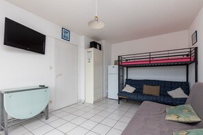 Quarto com cama de solteiro, escrivaninha, televisão e frigorífico.