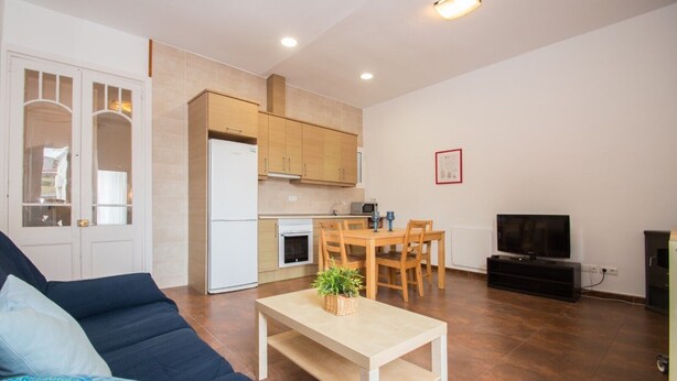 A living room with a sofa, a coffee table, a TV, and a kitchen area with cabinets and appliances. - Xaro Beach Apartment – Bright Family Apartment 2 Minutes from the Beach (Canet de Mar)