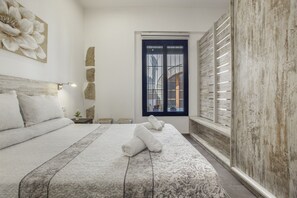 A bedroom with a large bed, a window with blinds, a wall-mounted lamp, and a decorative flower painting.