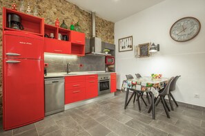 Une cuisine moderne avec des meubles de rangement rouges, un lave-vaisselle en acier inoxydable, un four à micro-ondes et un coin repas comprenant une table et des chaises.