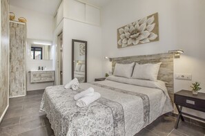 A bedroom with a large bed, a nightstand, a wall-mounted mirror, a wooden headboard, and a floral artwork. - Spectacular designer loft just five minutes' walk from the beach (Canet de Mar)