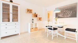 A dining area with a white table, chairs, and a pendant light. There is a cabinet with glass doors and a framed cityscape on the wall.